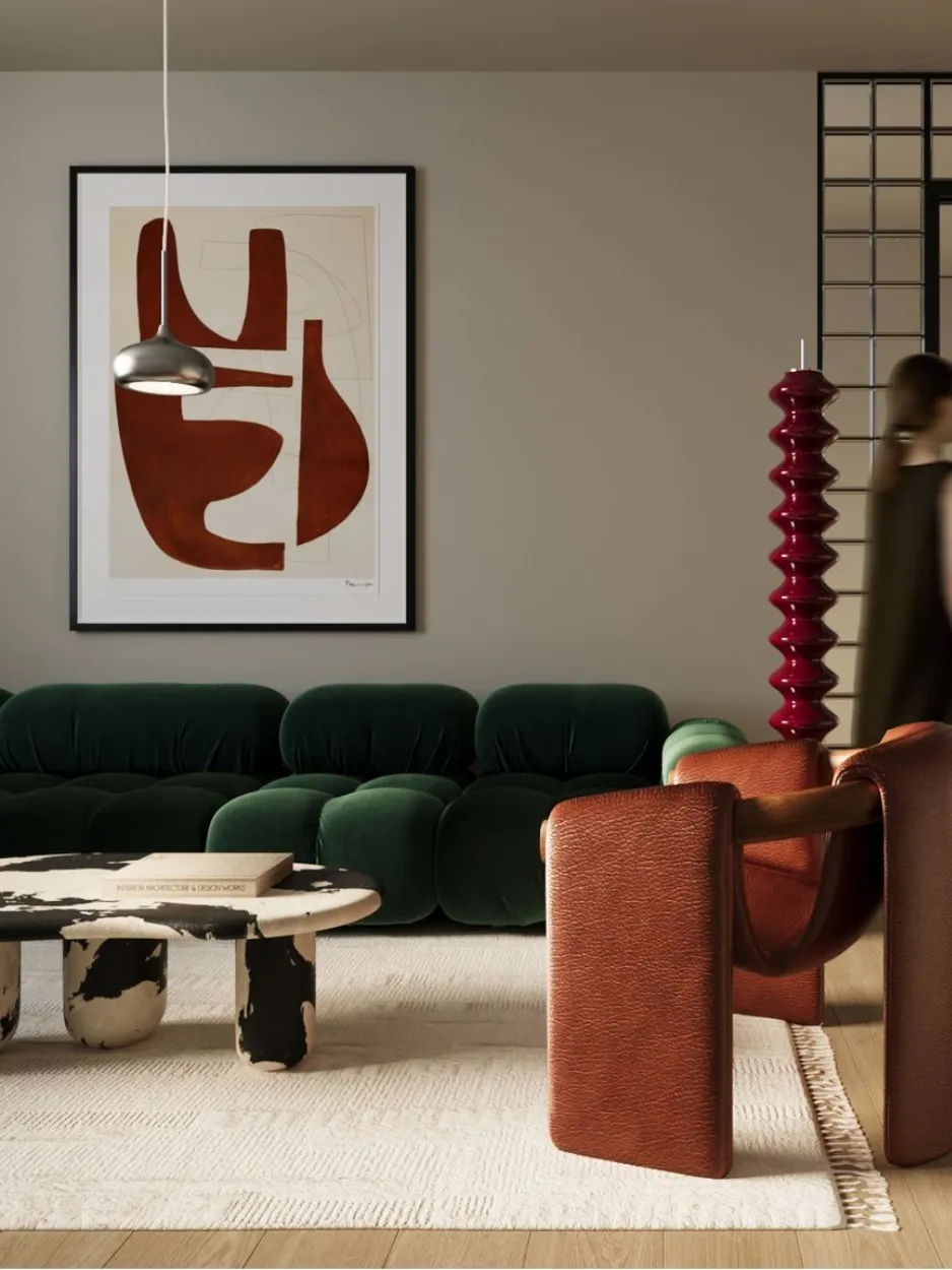 A modern living room with a green velvet sofa, a brown leather chair, a cowhide-patterned coffee table, abstract wall art, a red sculptural floor lamp, and a blurred person walking past a grid divider.