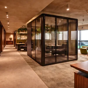 Modern office interior design and fit out by interioritalia features a glass-walled meeting room, open workstations, warm lighting, carpeted floors, and green plants hanging from the ceiling for a welcoming, professional atmosphere.