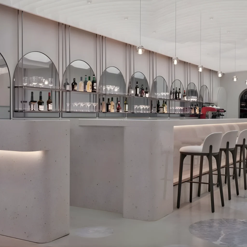 Modern bar interior with a curved counter, high stools, and a back wall displaying bottles and glassware under arched mirrors, with pendant lights hanging from the ceiling.