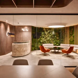 Modern office lobby with a marble reception desk, green vertical garden wall, circular white couch, and two orange chairs—an inviting space showcasing expert office interior design and fit out by interioritalia.